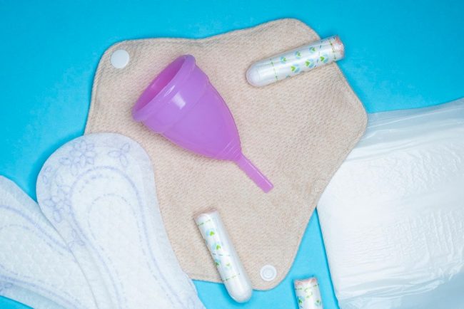 Menstrual products and supplies (pads, tampons, menstrual cups) on a colorful background.