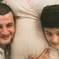A joyful family moment with father and son embracing the pregnant mother, symbolizing love and togetherness.