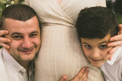 A joyful family moment with father and son embracing the pregnant mother, symbolizing love and togetherness.