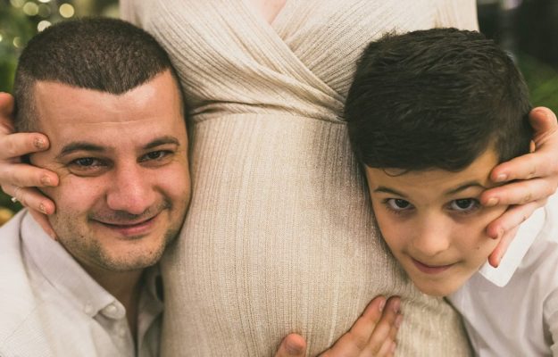 A joyful family moment with father and son embracing the pregnant mother, symbolizing love and togetherness.